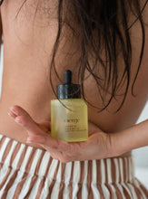 Load image into Gallery viewer, Woman holding hair and body oil bottle